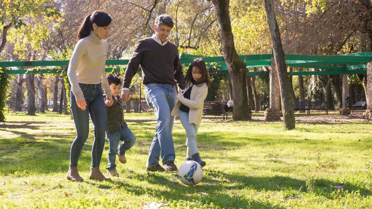 A family plays soccer together in a sunny park, enjoying quality time outdoors.